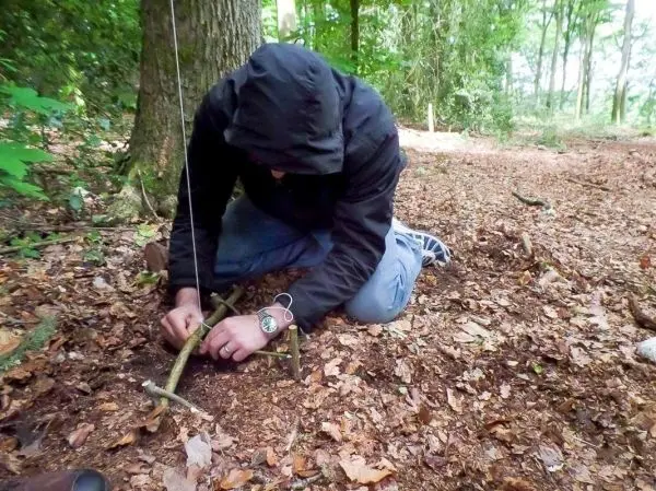 Person baut eine Konstruktion aus Ästen im Wald