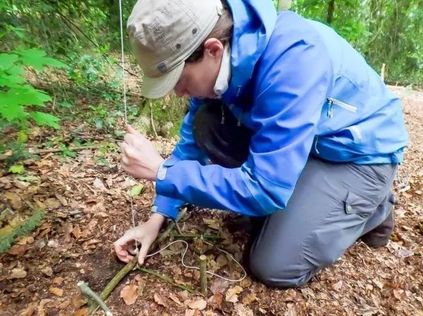 Person befestigt eine Schnur an einem Stock im Wald
