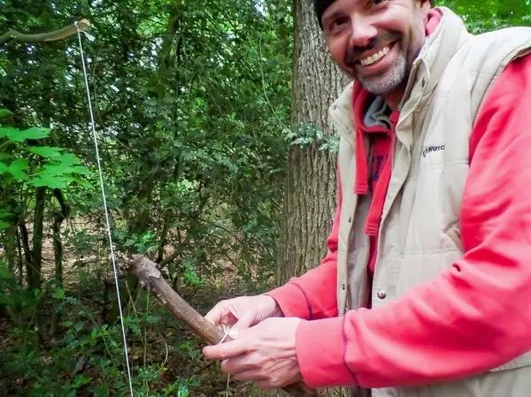Person bindet Schnur an Stock im Wald