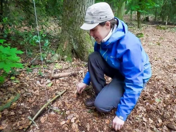 Person kniet im Wald und richtet eine Falle aus