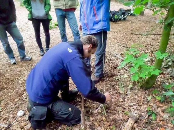 Person knotet eine Schnur an einem Stock im Wald