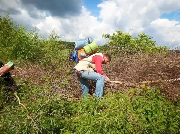 Person mit Rucksack schneidet einen Stock im Unterholz