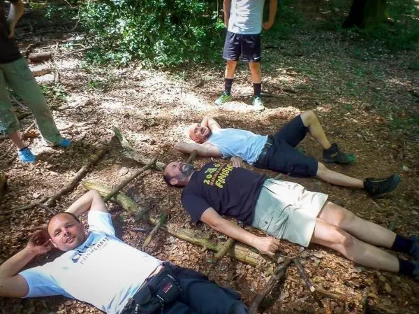 Drei Personen liegen auf einem Untergrund aus Ästen im Wald