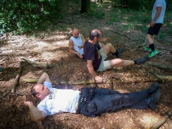 Drei Personen liegen und sitzen auf dem Boden aus Laub und Ästen im Wald