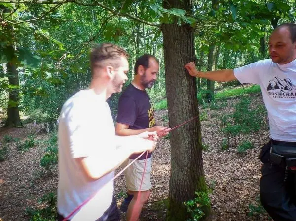 Drei Personen spannen ein Seil um einen Baum im Wald