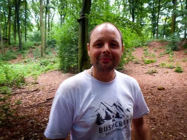 Ein Mann steht im Wald mit grünen Bäumen und Laubboden