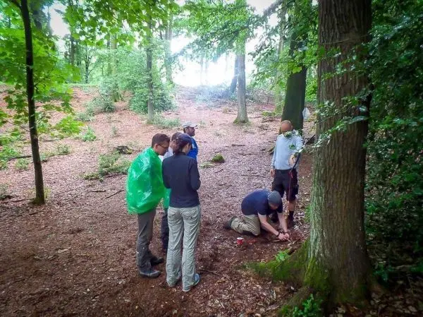 Gruppe arbeitet am Boden im Wald, einer bearbeitet den Untergrund mit einem Werkzeug