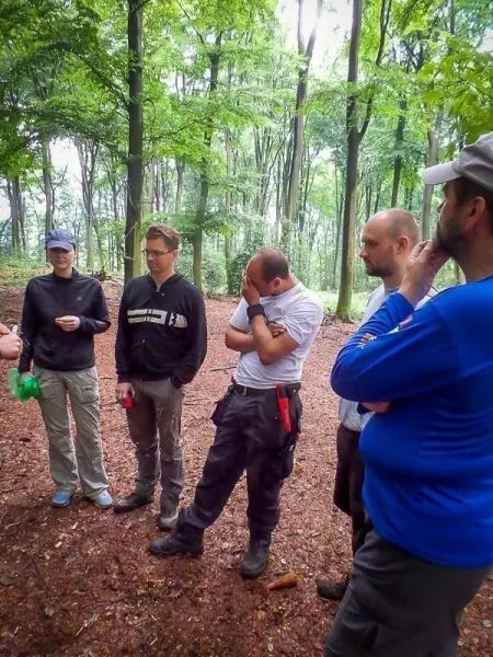 Gruppe diskutiert im Wald, einige Personen hören aufmerksam zu