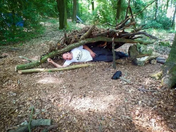 Improvisierte Tarp-Notunterkunft aus Ästen im Wald, Person liegt darunter