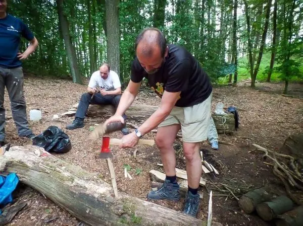 Mann bearbeitet Holzstück mit Axt auf dem Boden im Wald