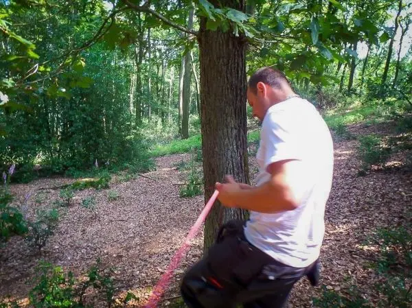 Mann befestigt ein pinkes Seil an einem Baumstamm im Wald