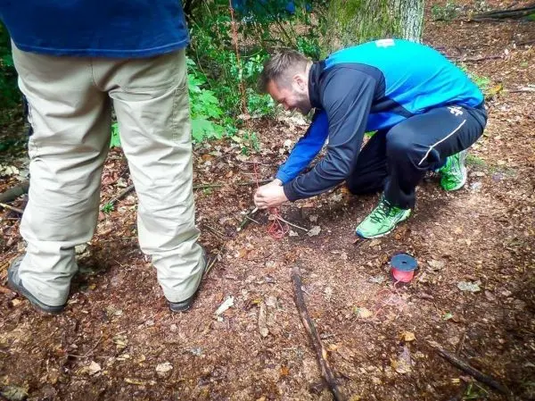 Mann bindet Schnüre an Äste zur Konstruktion einer Falle im Wald