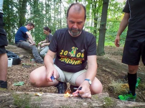 Mann entzündet Zunder mit Feuerstahl auf einem Baumstamm im Wald