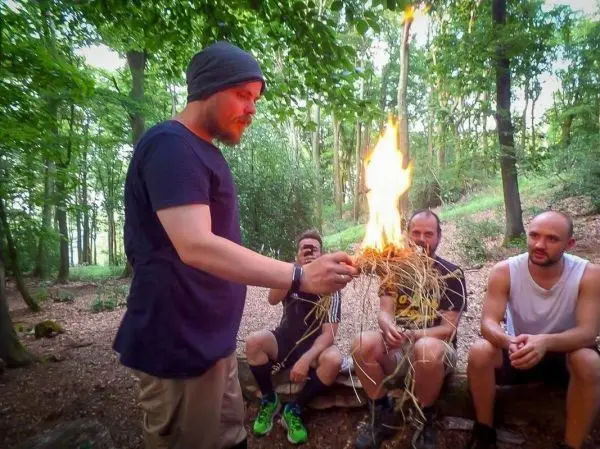 Mann hält brennendes Zundernest in der Hand, während andere zuschauen