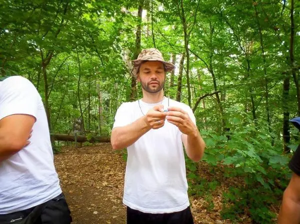 Mann hält ein kleines Objekt in den Händen, umgeben von Bäumen und Laub