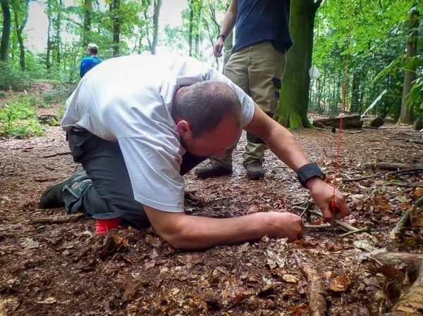 Mann kniet im Wald und baut eine Schlagfalle aus Ästen
