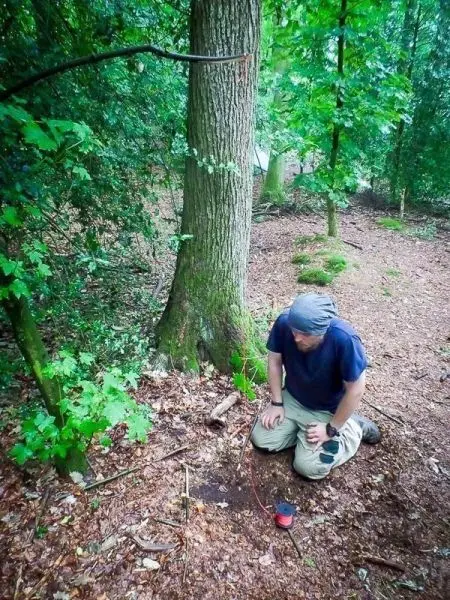 Mann kniet neben einem Baum und richtet eine Schlagfalle ein
