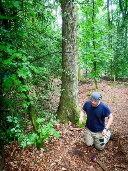 Mann kniet neben einer selbstgebauten Seilbrücke zwischen zwei Bäumen