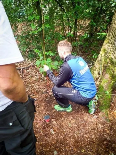 Mann kniet sich im Wald und untersucht den Boden neben einem Baum