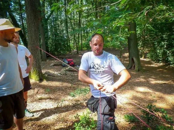 Mann knotet ein Seil in einem Waldgebiet, während andere zuschauen