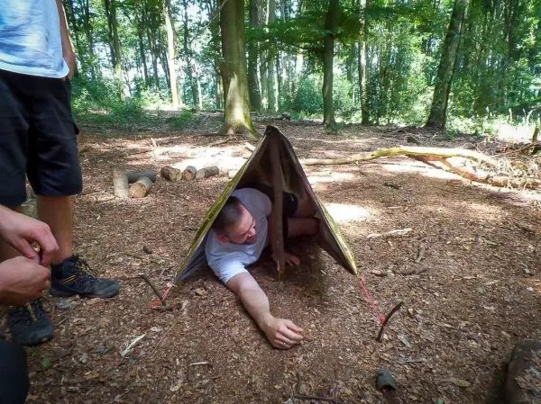 Mann kriecht aus einer Tarp-Notunterkunft im Wald