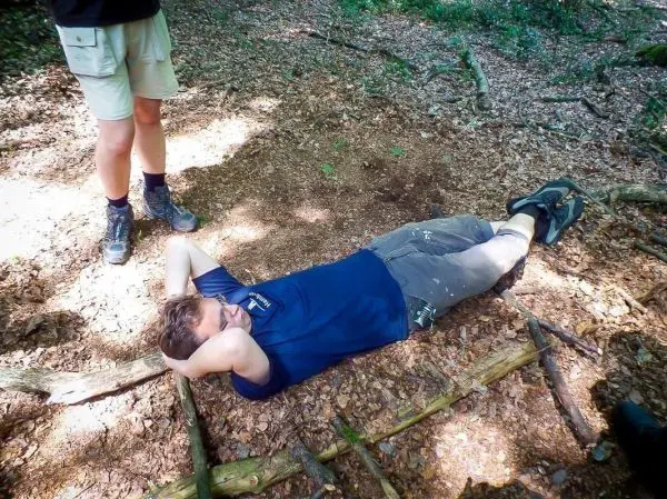 Mann liegt auf dem Boden im Wald, Hände hinter dem Kopf verschränkt