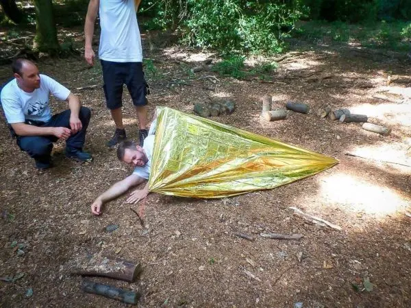 Mann liegt in einer Rettungsdecke auf dem Boden, zwei Personen beobachten ihn