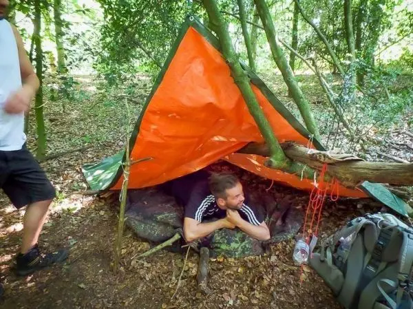 Mann liegt in einer Tarp-Notunterkunft aus orangefarbener Plane zwischen Bäumen