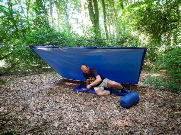 Mann sitzt unter einer Tarp-Notunterkunft und bereitet seine Ausrüstung vor