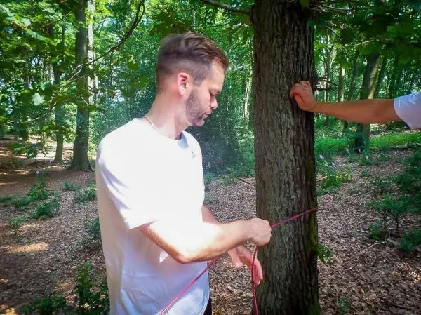 Person bindet ein Seil um einen Baumstamm