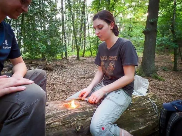 Person entzündet Feuer auf einem Baumstamm beim Survival Training