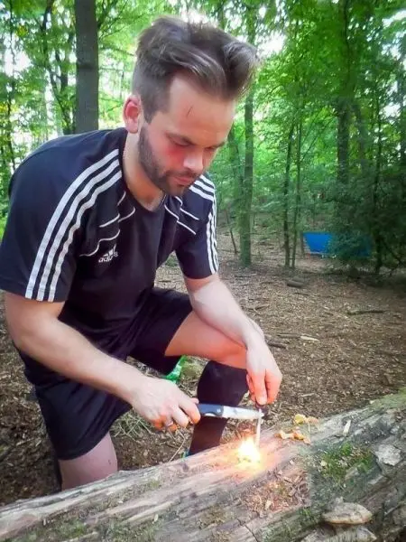Person entzündet Feuer mit einem Feuerstahl auf einem Baumstamm beim Survival Training