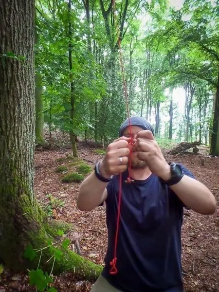 Person knotet ein rotes Seil im Wald