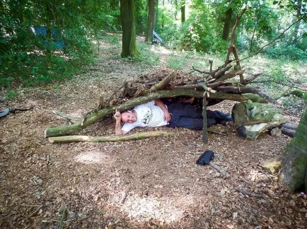 Person liegt unter einer selbstgebauten Unterkunft aus Ästen im Wald