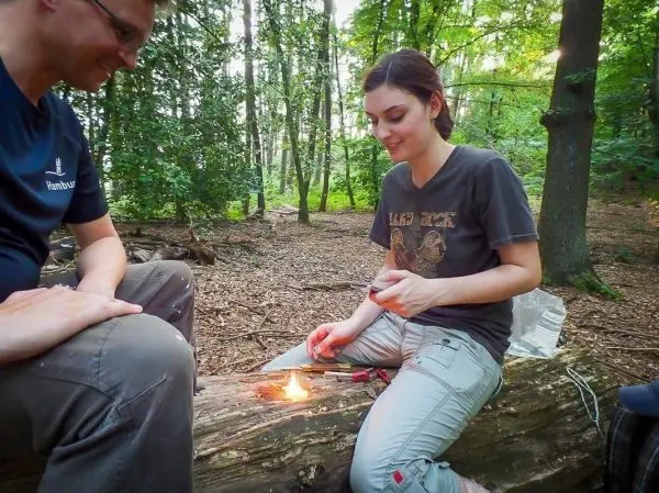 Person zündet Feuer auf einem Baumstamm im Wald an beim Survival Training