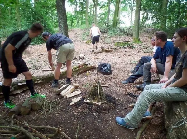 Personen sammeln Holz und bereiten ein Feuer im Wald vor beim Survival Training
