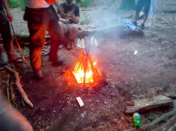 Personen sitzen um ein Feuer im Wald beim Überlebenstraining