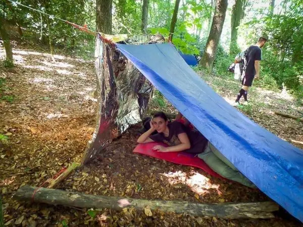 Tarp-Notunterkunft aus Folie und Plane mit Person auf Unterlage im Inneren