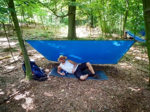 Tarp-Notunterkunft hängt zwischen zwei Bäumen, Person liegt entspannt darunter