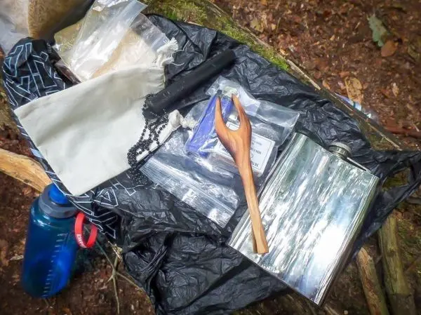 Verschiedene Ausrüstungsgegenstände liegen auf einem schwarzen Tuch im Wald