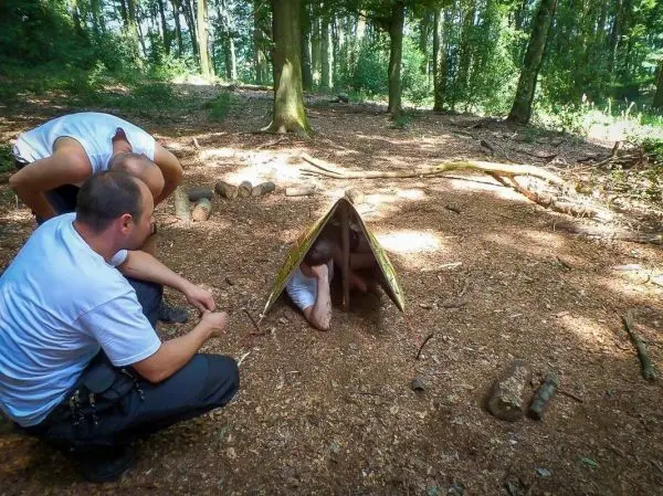 Zwei Personen beobachten eine Tarp-Notunterkunft im Wald