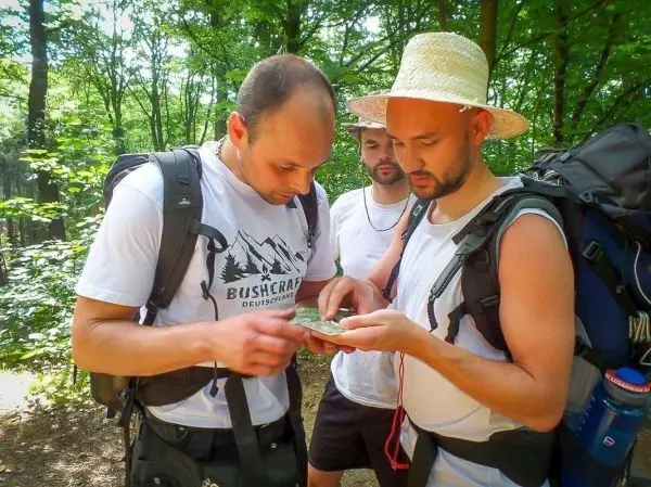 Zwei Personen betrachten eine Karte im Wald, während eine dritte Person zuschaut