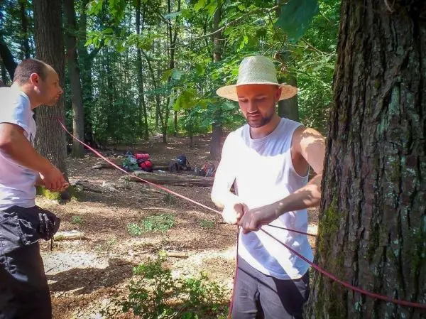 Zwei Personen binden ein Seil um einen Baum im Wald