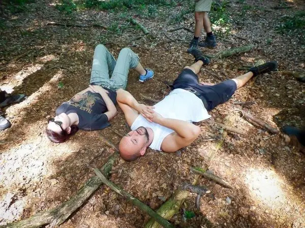 Zwei Personen liegen auf dem Waldboden zwischen Ästen und Laub