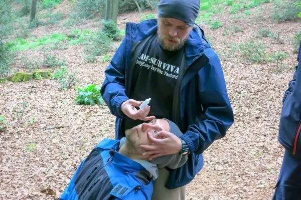 Erste-Hilfe-Maßnahme mit Spray auf das Gesicht einer liegenden Person im Wald