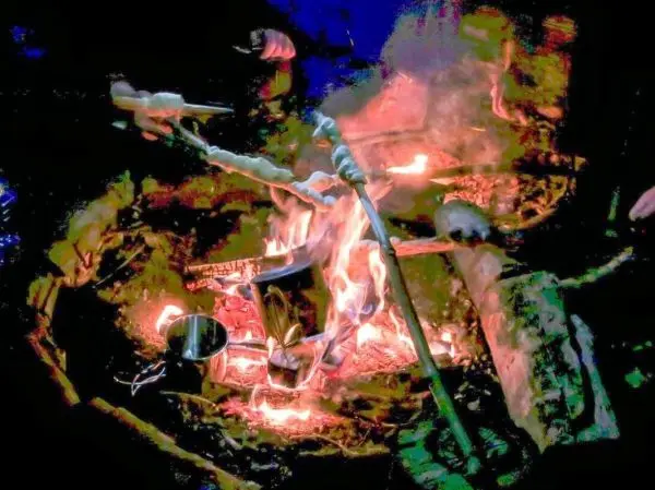 Feuer brennt in einer Feuerstelle mit Kochgeschirr darüber beim Survival Training