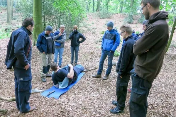 Gruppe beobachtet Erste-Hilfe-Übung auf einer Matte im Wald
