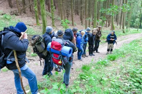 Gruppe mit Rucksäcken hört einem Trainer im Wald zu