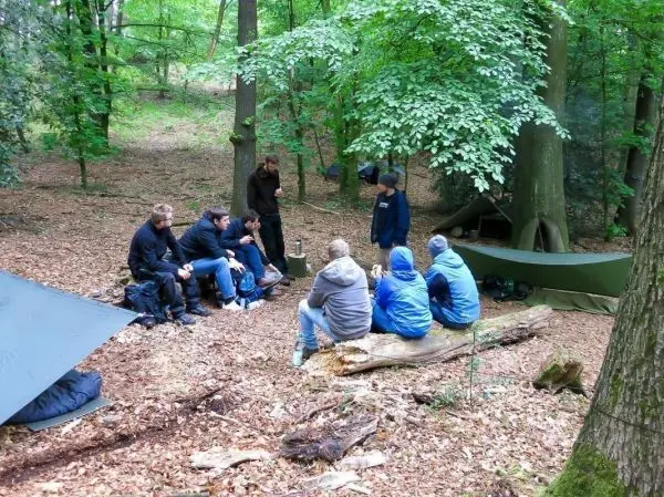 Gruppe sitzt auf Baumstamm und diskutiert in bewaldeter Umgebung