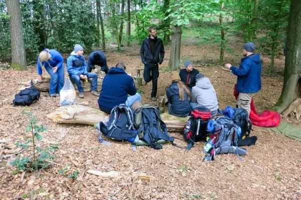 Gruppe sitzt auf einem Baumstamm im Wald, Rucksäcke liegen verstreut